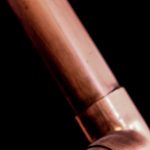 Industrial copper pipes close-up with a dark background, highlighting metallic textures.